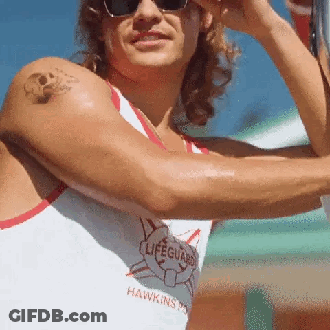 A Man With A Tattoo On His Arm Is Wearing Sunglasses And A Lifeguard Shirt . GIF