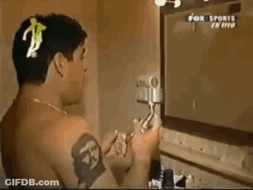 A Man With A Tattoo On His Arm Looks At Himself In A Mirror While Fox Sports Is Playing GIF