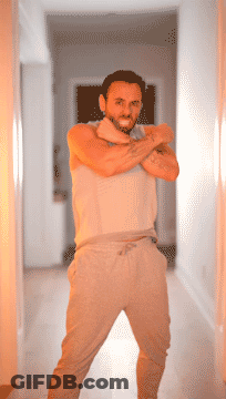 A Man With A Tattoo On His Arm Stands In A Hallway With His Arms Crossed GIF
