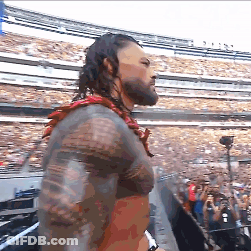 A Man With A Tattoo On His Arm Stands In Front Of A Crowd GIF