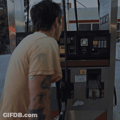 A Man With A Tattoo On His Arm Stands In Front Of A Gas Pump That Says T8 On It GIF