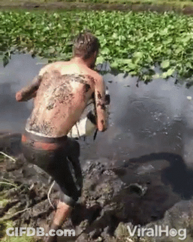 A Man With A Tattoo On His Back Is Walking Through The Mud . GIF