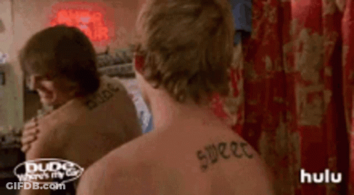 A Man With A Tattoo On His Back Looks At Himself In A Mirror . GIF