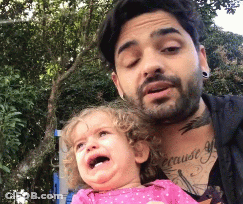 A Man With A Tattoo On His Chest Is Holding A Crying Baby GIF