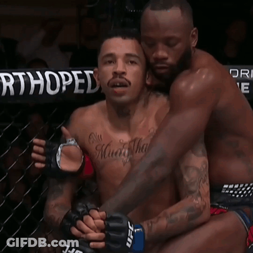 A Man With A Tattoo On His Chest Is Hugging Another Man With Ufc Gloves GIF