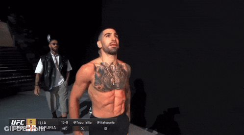 A Man With A Tattoo On His Chest Is Standing In Front Of A Ufc Advertisement GIF