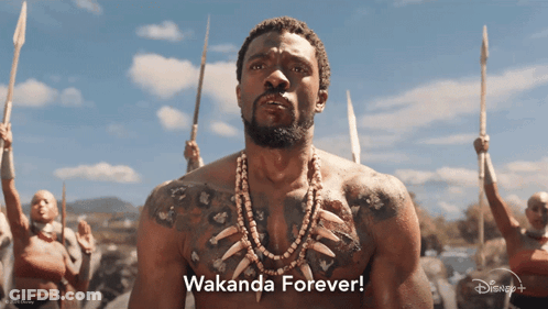 A Man With A Tattoo On His Chest Stands In Front Of A Group Of People Holding Spears And Says " Wakanda Forever " GIF
