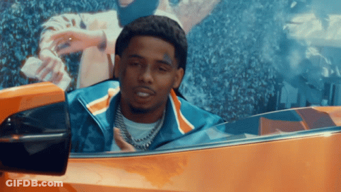 A Man With A Tattoo On His Face Is Driving An Orange Car GIF