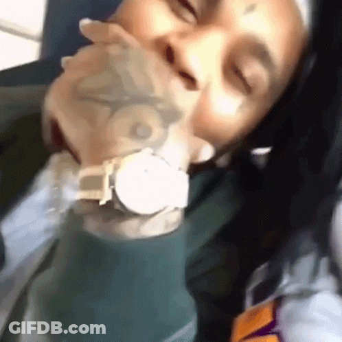 A Man With A Tattoo On His Face Is Holding A Watch In His Mouth . GIF