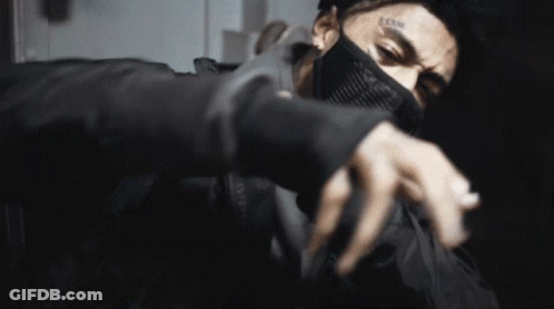A Man With A Tattoo On His Face Is Wearing A Mask And A Ring On His Finger . GIF