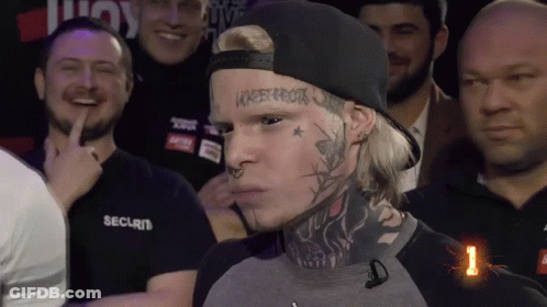 A Man With A Tattoo On His Face Stands In Front Of A Crowd Of People Wearing Security Shirts GIF