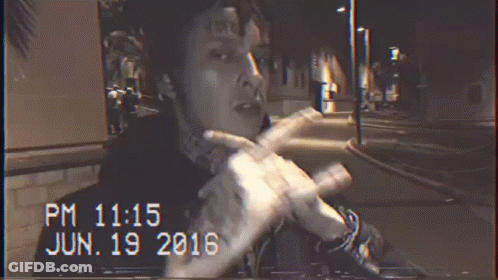 A Man With A Tattoo On His Forehead Is Smoking A Cigarette At Night GIF