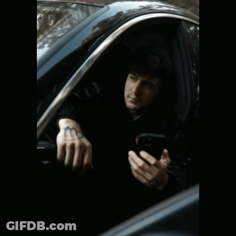 A Man With A Tattoo On His Hand Is Sitting In A Car And Looking At His Phone GIF