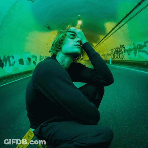 A Man With A Tattoo On His Neck Is Kneeling Down In Front Of A Green Tunnel GIF