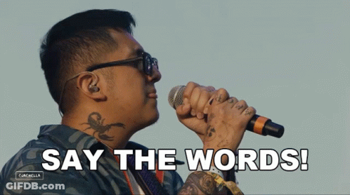A Man With A Tattoo On His Neck Is Singing Into A Microphone With The Words Say The Words Behind Him GIF