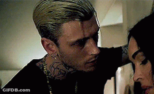A Man With A Tattoo On His Neck Is Standing Next To A Woman . GIF