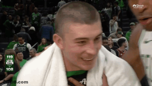 A Man With A Towel Around His Neck Is Smiling In Front Of A Scoreboard That Says 108 On It GIF