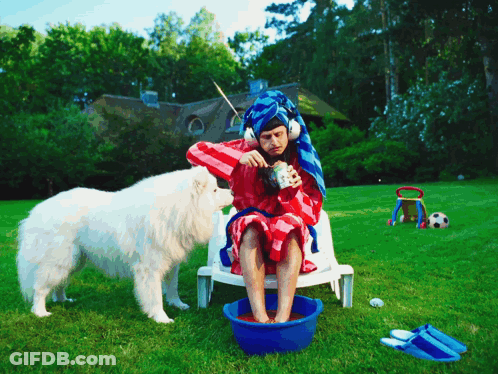 A Man With A Towel Wrapped Around His Head Sits In A Chair With A Dog GIF