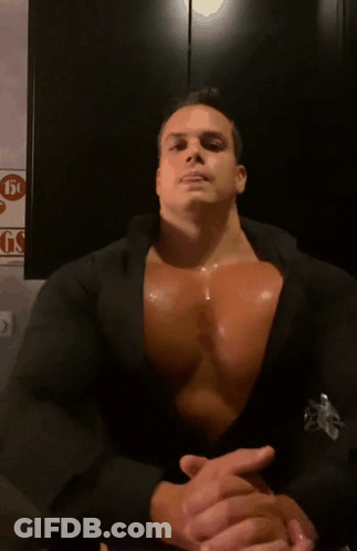 A Man With A Very Large Chest Is Sitting In Front Of A Sign That Says Gs GIF