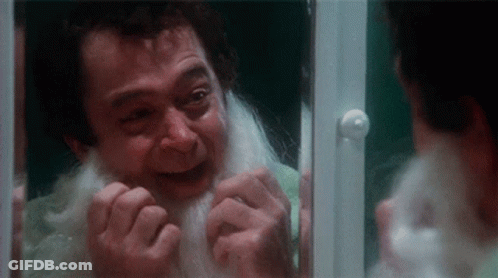 A Man With A White Beard Is Looking At Himself In A Mirror . GIF