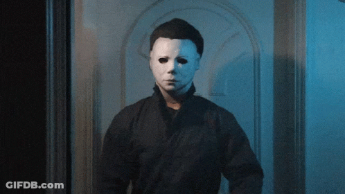 A Man With A White Mask On His Face Stands In Front Of A Door GIF