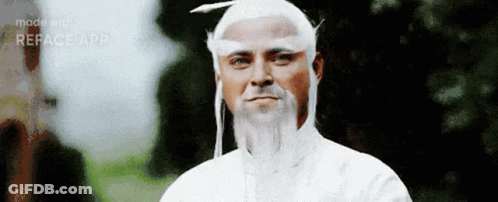 A Man With A White Wig And Beard Is Standing In Front Of A Forest . GIF