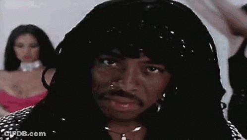 A Man With A Wig And A Mustache Is Standing In Front Of A Woman In A Pink Dress . GIF