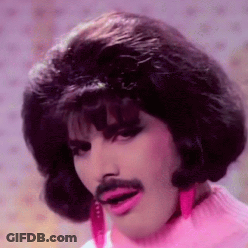 A Man With A Wig And Mustache Is Wearing A Pink Sweater And Pink Earrings . GIF