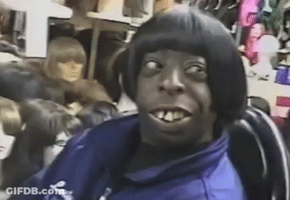 A Man With A Wig On His Head Is Sitting In A Chair In Front Of A Mannequin . GIF