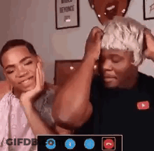 A Man With A Wig On His Head Is Sitting Next To A Woman . GIF