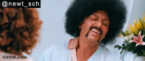 A Man With An Afro And Mustache Is Talking To A Woman In A Room . GIF