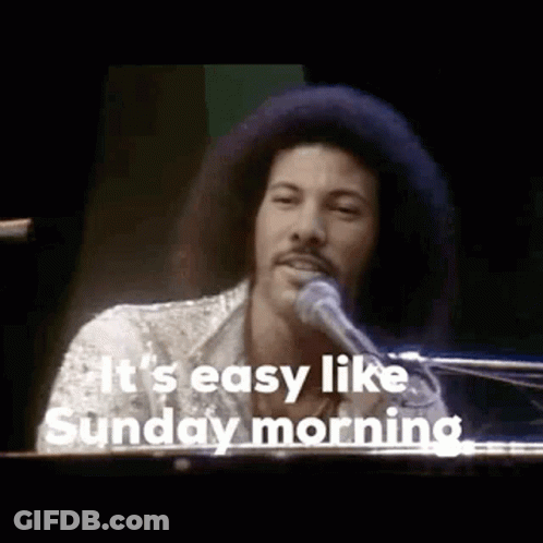 A Man With An Afro Is Singing Into A Microphone While Playing A Piano . GIF