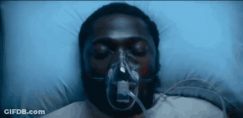 A Man With An Oxygen Mask On His Face Is Laying In A Hospital Bed GIF