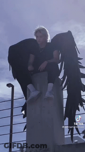 A Man With Angel Wings Is Sitting On A Concrete Wall GIF