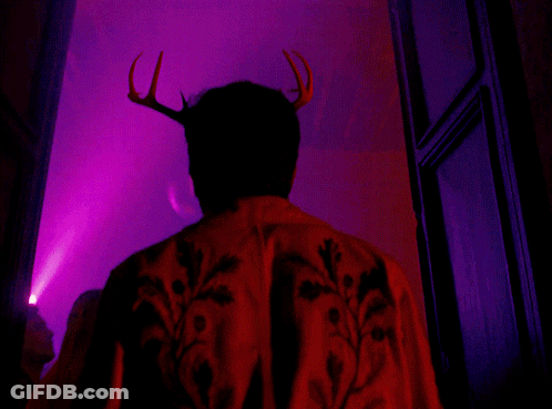 A Man With Antlers On His Head Is Standing In Front Of A Pink Light GIF
