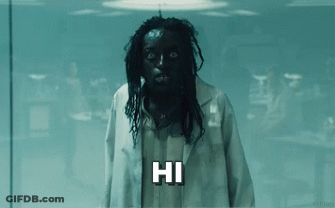 A Man With Black Hair And Dreadlocks Is Wearing A Lab Coat And A Mask And Saying Hi . GIF
