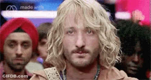 A Man With Blonde Curly Hair And A Beard Is Standing In Front Of A Crowd Of People . GIF