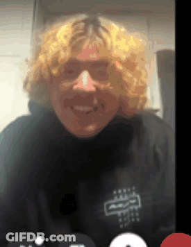 A Man With Blonde Curly Hair Is Smiling While Wearing A Black Shirt With The Letter R On It GIF