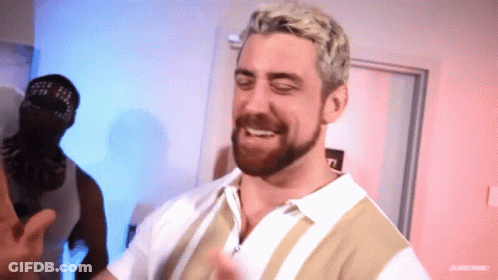 A Man With Blonde Hair And A Beard Is Smiling In Front Of A Door GIF