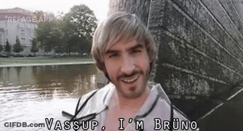A Man With Blonde Hair And A Beard Is Standing Next To A Body Of Water And Smiling . GIF
