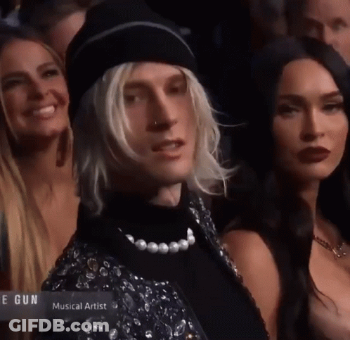 A Man With Blonde Hair And A Pearl Necklace Is Standing In A Crowd Of People With The Word Musical Artist On The Bottom GIF