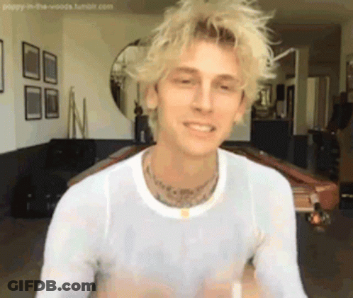 A Man With Blonde Hair And A White Shirt Is Sitting In A Living Room Next To A Pool Table . GIF