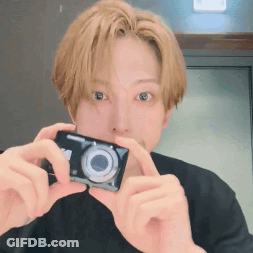 A Man With Blonde Hair Is Holding A Camera In Front Of His Face GIF