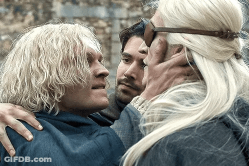 A Man With Blonde Hair Is Hugging Another Man And A Woman GIF