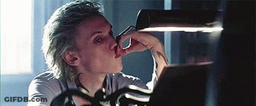 A Man With Blonde Hair Is Licking His Nose While Looking At A Mirror . GIF