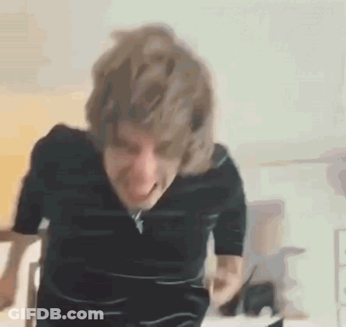 A Man With Blonde Hair Is Making A Funny Face While Standing In Front Of A Table . GIF