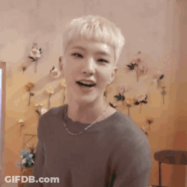 A Man With Blonde Hair Is Smiling In Front Of A Wall With Flowers On It . GIF