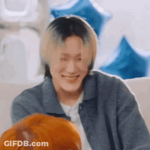 A Man With Blonde Hair Is Smiling While Sitting On A Couch With Balloons In The Background . GIF