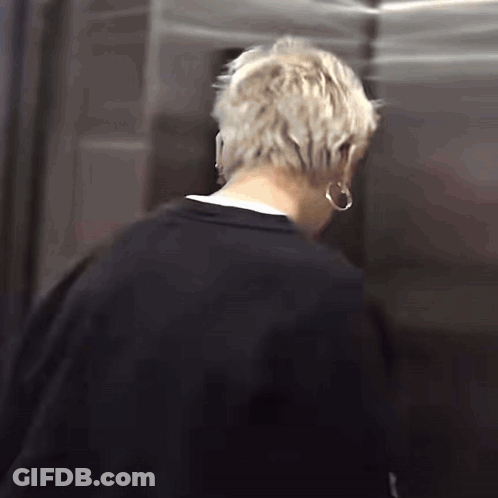 A Man With Blonde Hair Is Standing In An Elevator Wearing Hoop Earrings . GIF