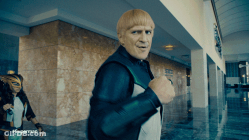 A Man With Blonde Hair Is Walking In A Hallway With The Hashtag #Superman GIF